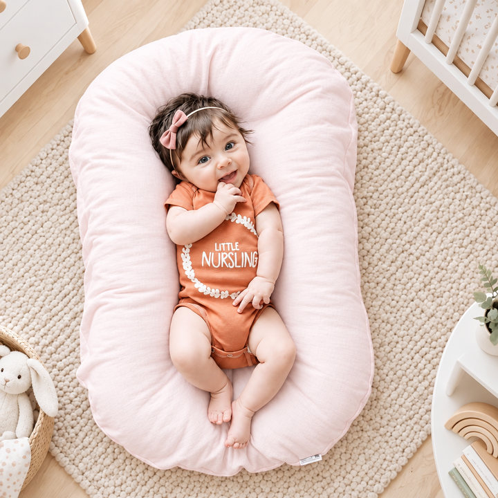 Smiling baby with a pink hair bow lies on a pale pink support pillow in a nursery 1