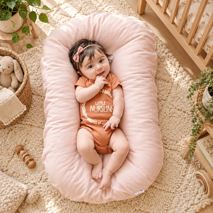 Baby in a headband lying on a pale pink oval support pillow in a nursery 1