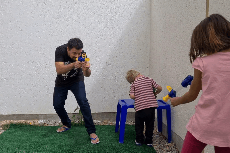 Man and two children play with the launchers in a small courtyard, one child bending over a blue stool 10