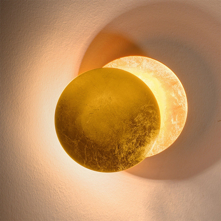Close-up of the gold-leaf front disc overlapping the softly glowing rear disc on a textured wall 11