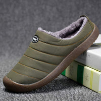 Single olive green slipper tilted against a stack of books, showing stitched quilted panels and thick brown sole 4