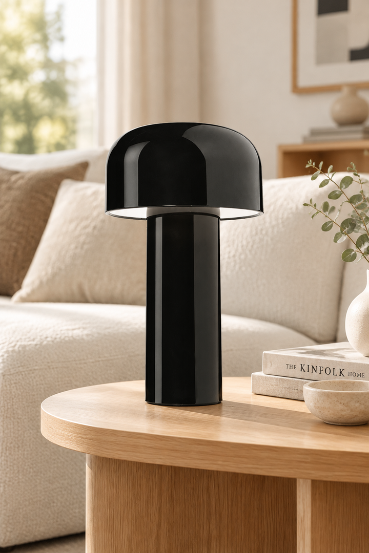 Glossy black mushroom lamp on an oak coffee table next to books and a bowl, with a cream sofa behind 30