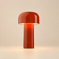 Glossy red mushroom-shaped lamp glowing under its shade on a cream background, button visible on the stem 29