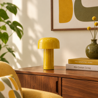 Glossy yellow mushroom lamp on a walnut sideboard beside books, a vase and a yellow armchair 1