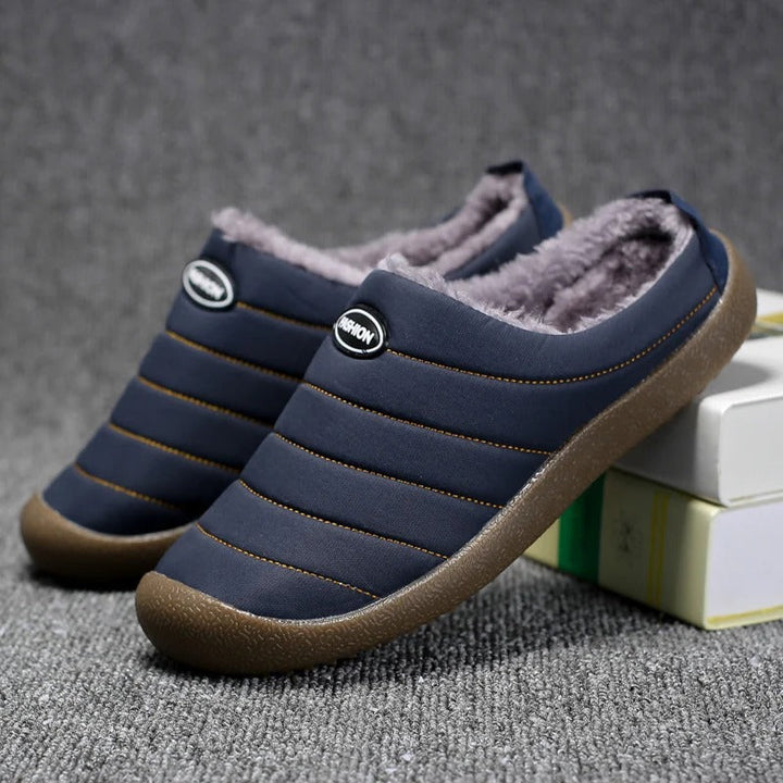 Navy blue quilted slippers with fluffy grey lining resting against stacked books on grey carpet 5