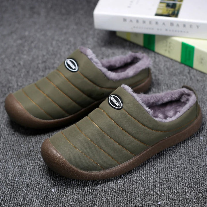 Pair of olive green quilted slippers with grey fleece lining on a grey carpet beside books 1