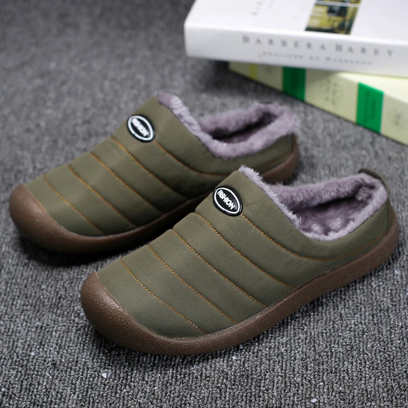 Pair of olive green quilted slippers with grey fleece lining, resting on grey carpet beside books 2