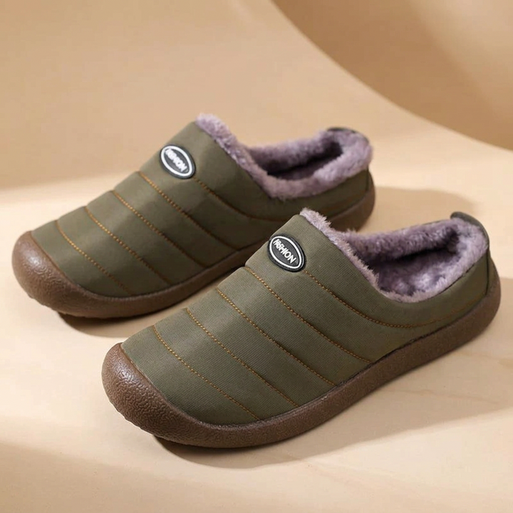 Pair of olive green quilted slippers with purple-grey fleece lining on a beige curved backdrop 17