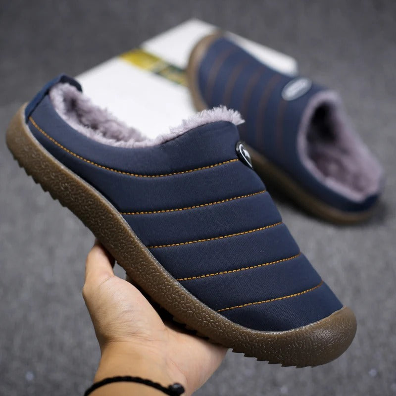 Hand holding a navy blue slipper, showing its stitched quilted stripes, fleece lining and textured sole 5