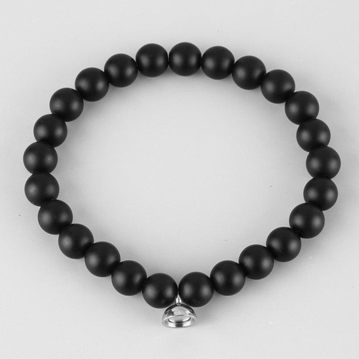 Matte black round bead stretch bracelet with a small silver magnetic charm, on a light grey background 2