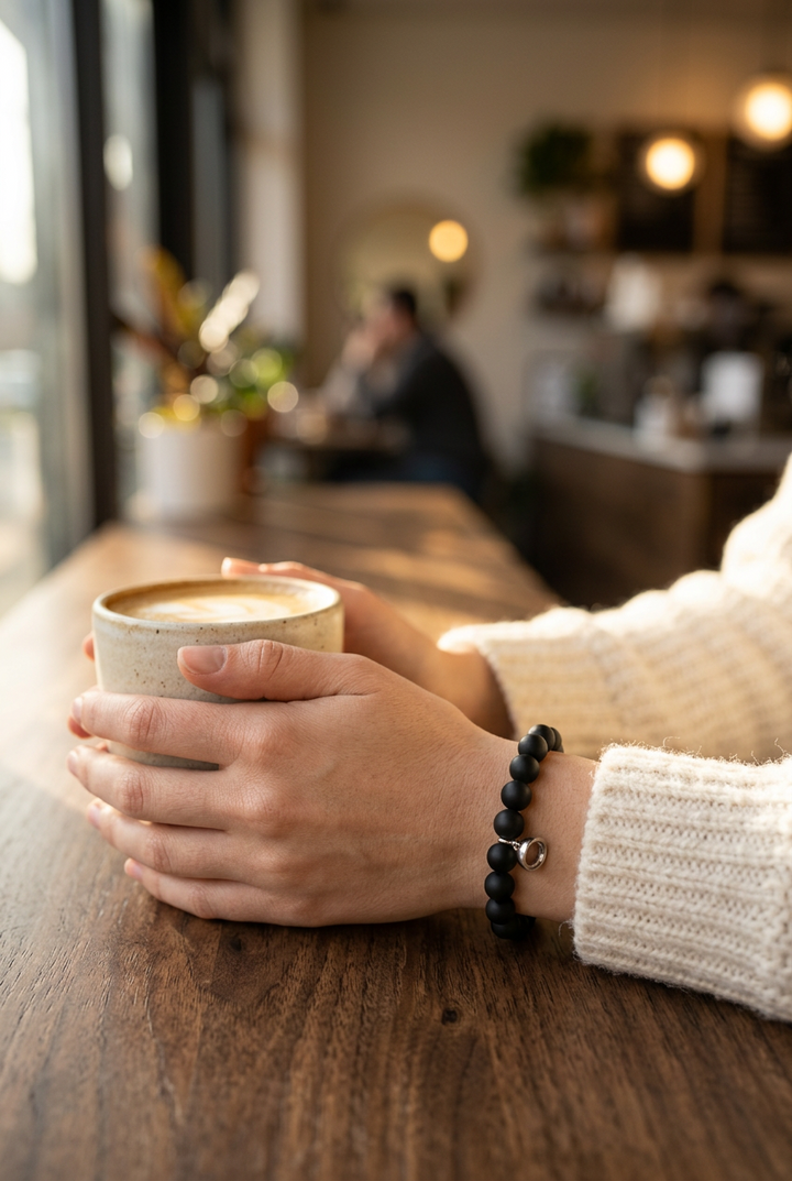 Black beaded bracelet with a small silver charm on a wrist holding a latte in a cafe 1