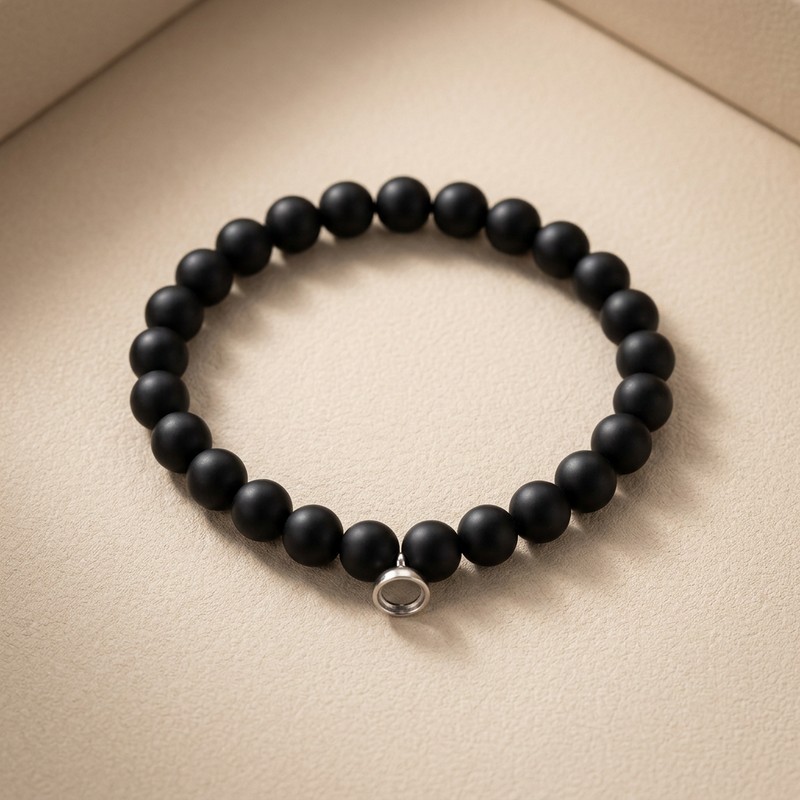 Stretch bracelet of matte black round beads with a small silver magnetic clasp, laid on beige card 1