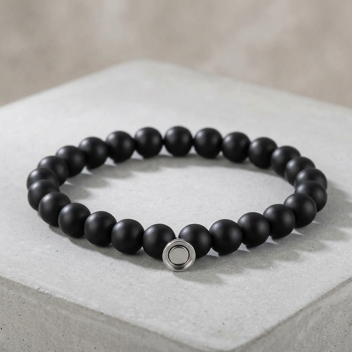 Matte black bead bracelet with silver round magnetic clasp resting on a pale concrete block 2