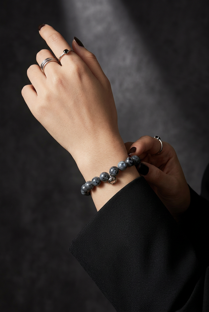Woman's wrist wearing the grey speckled bead bracelet, with silver rings and a black sleeve 4