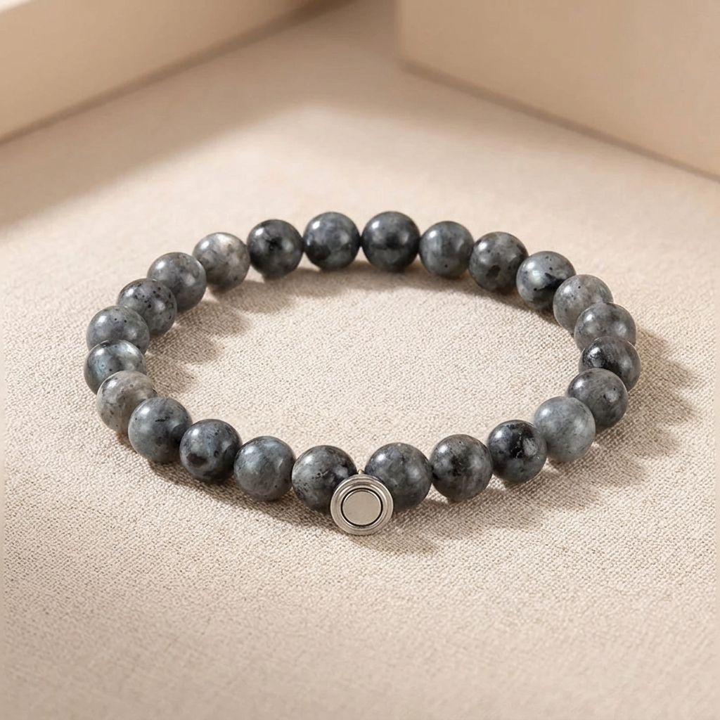 Bracelet of dark grey speckled stone beads with a round silver magnetic clasp, resting on a beige surface 3