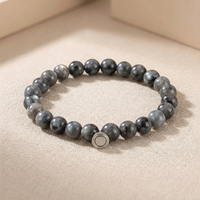 Bracelet of dark grey speckled stone beads with a round silver magnetic clasp, resting on a beige surface 3