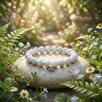 White marbled bead bracelet with a silver magnetic clasp resting on a pale stone among ferns and small flowers 1