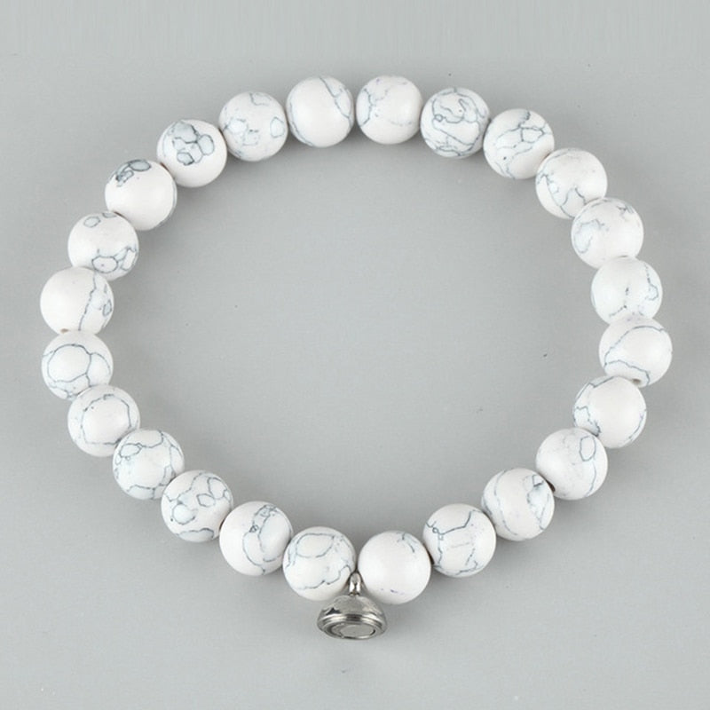 White bead bracelet with grey marbled veining and a small silver magnetic charm, on a grey background 3