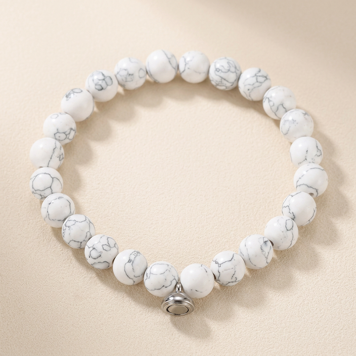 Bracelet of white beads with grey marbled veining and a silver magnetic clasp, on a cream background 2