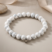 White bead bracelet with grey marbled veining and silver clasp, beside a pebble and cream ribbon 3