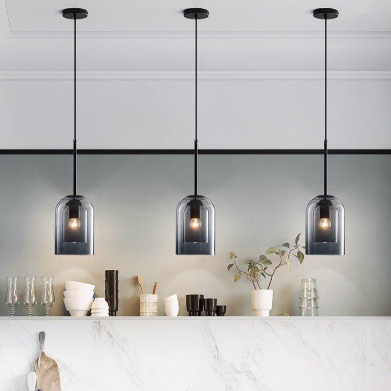 Row of three smoke grey pendants above a white marble counter with bowls, glasses and a plant 5