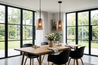 Two amber glass pendants hang above a wooden dining table with black chairs by large glazed doors 1