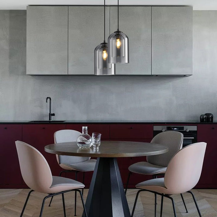 Two smoke grey pendants hanging at different heights over a round table with pink chairs 7