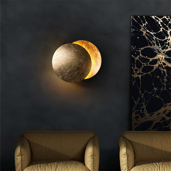 Gold moon lamp lit on a dark wall between two armchairs, beside marbled artwork 6