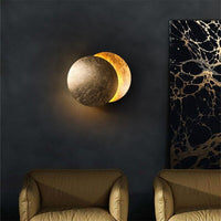 Lamp with a textured gold front disc above two armchairs, beside a marbled black and gold artwork 6
