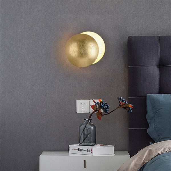 Gold wall lamp lit above a white bedside table with a vase of berries, beside a bed 6