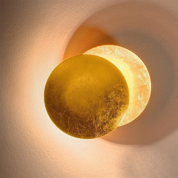 Gold disc lamp turned over a second glowing disc on a cream textured wall 11