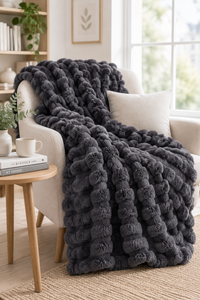 Dark grey bubble-textured blanket draped over a cream armchair beside a wooden side table 14