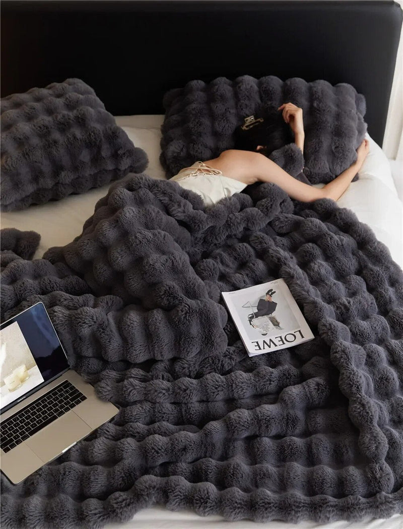 Dark grey fluffy blanket covers a bed with a laptop and magazine resting on top 3
