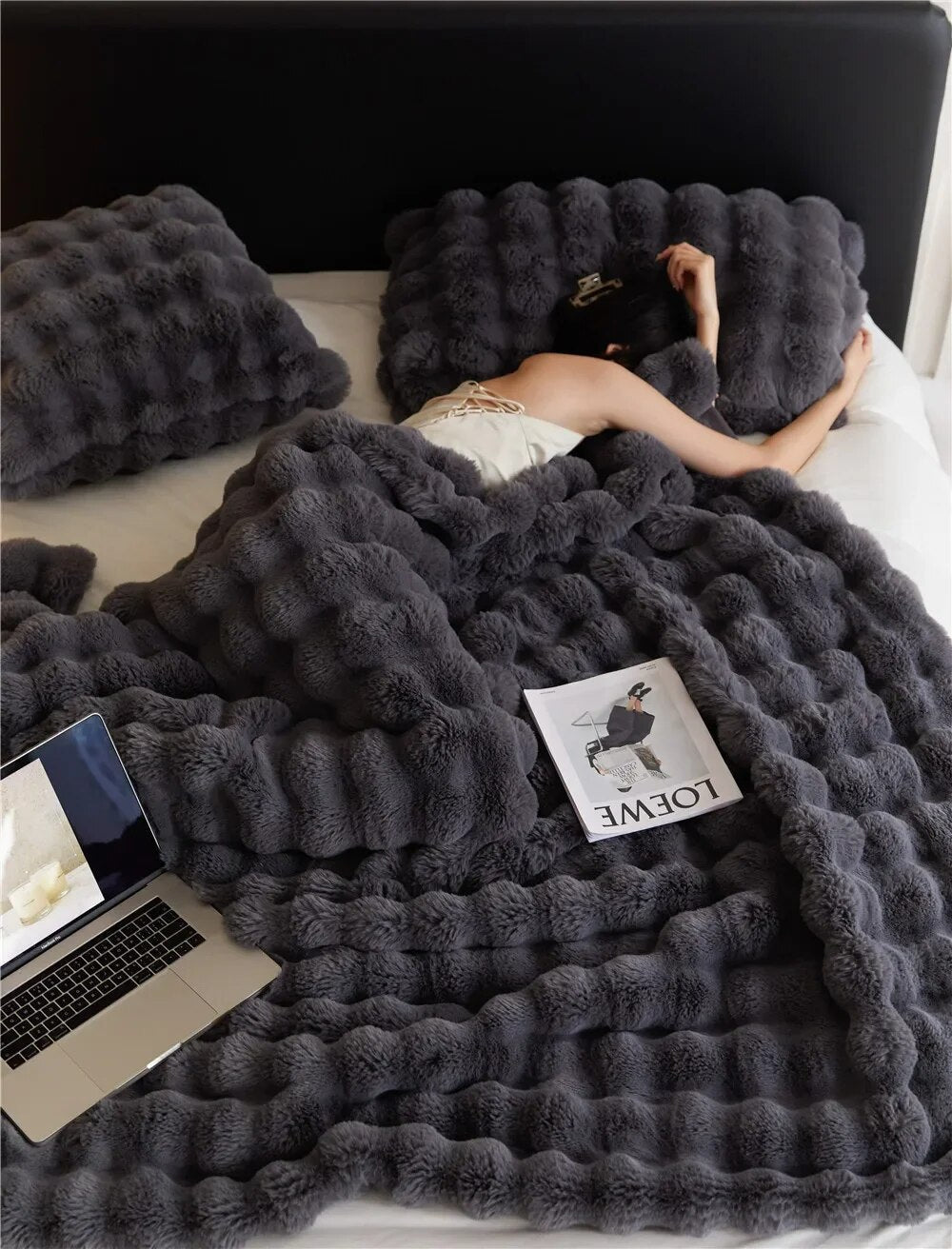 Dark grey bubble-textured plush blanket covering a sleeping woman on a bed, with a laptop and magazine nearby 2