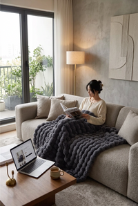 Woman reading a magazine on a cream sofa under a dark grey bubble-textured fluffy blanket 1