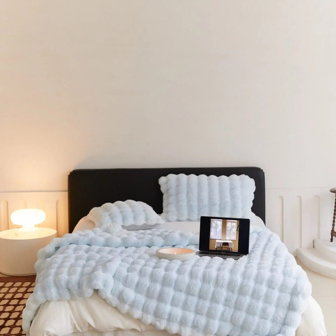 Pale blue bubble-textured blanket and matching pillows on a bed with a black headboard, laptop and candle 6