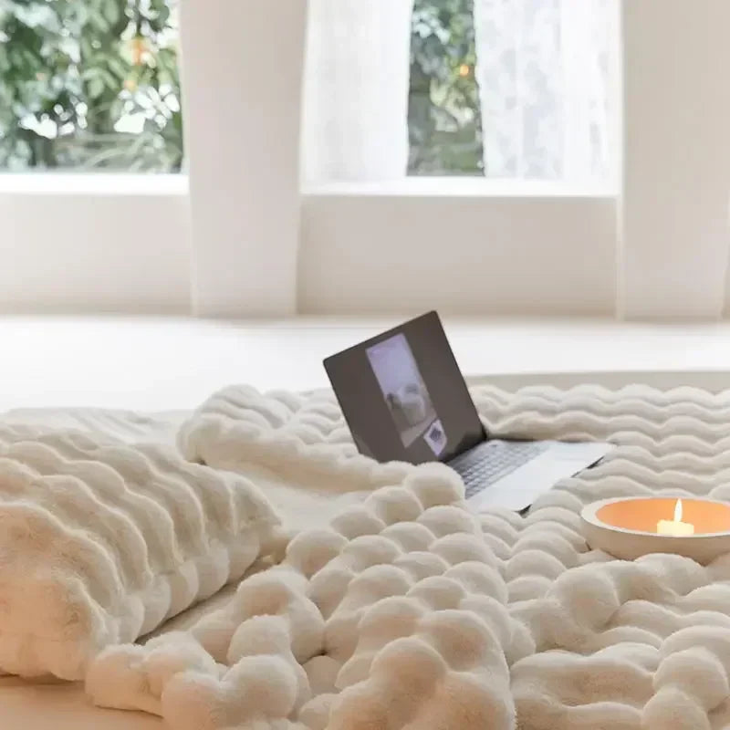 Close view of a cream plush blanket on a bed with a laptop and candle in front of a window 7