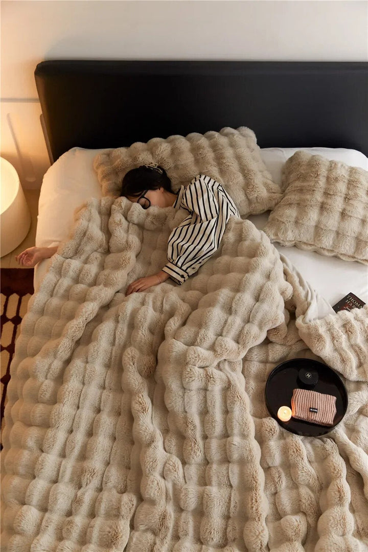 Overhead view of a woman asleep under a beige bubble-textured faux fur blanket with matching pillows 2
