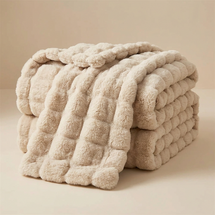 Beige bubble-textured fluffy blanket folded and draped over itself against a neutral studio backdrop 13