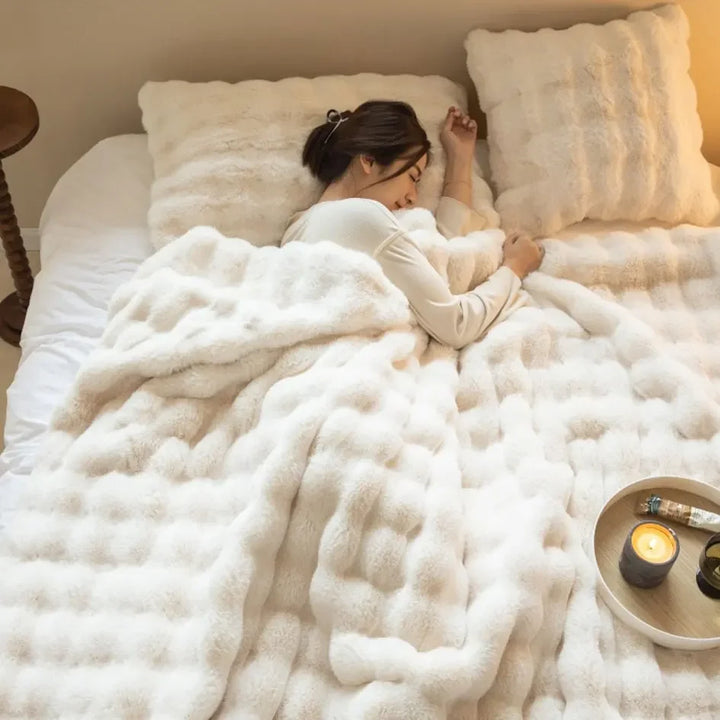 Woman sleeping under a cream white fluffy blanket with matching pillows and a lit candle on a tray 5