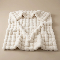 Cream white bubble-textured blanket laid flat with softly rippled folds on a plain beige background 16