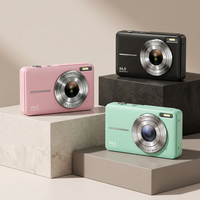 Pink, black and mint green compact cameras displayed on stone and concrete blocks against a beige backdrop 1