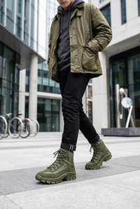 Man in olive jacket and black jeans walking in olive green lace-up high-top boots outdoors 1