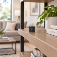 Small black cube camera sitting on a wooden shelf in a bright, cosy living room 1
