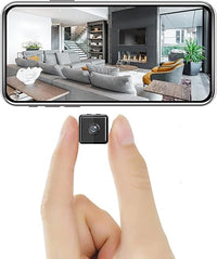 Tiny black cube camera held between finger and thumb, with a living room view on a phone above 2