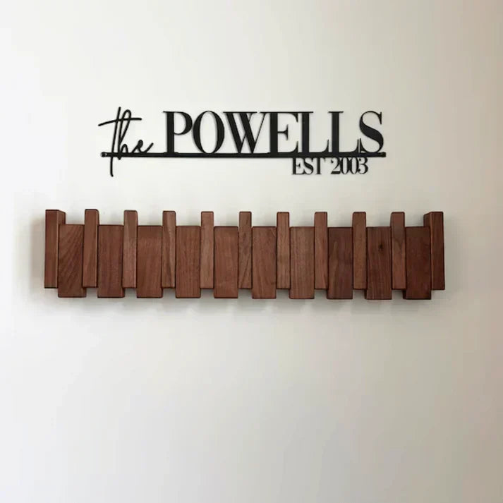 Dark wooden rack with all hooks folded flat, mounted below a black personalised family-name sign 6